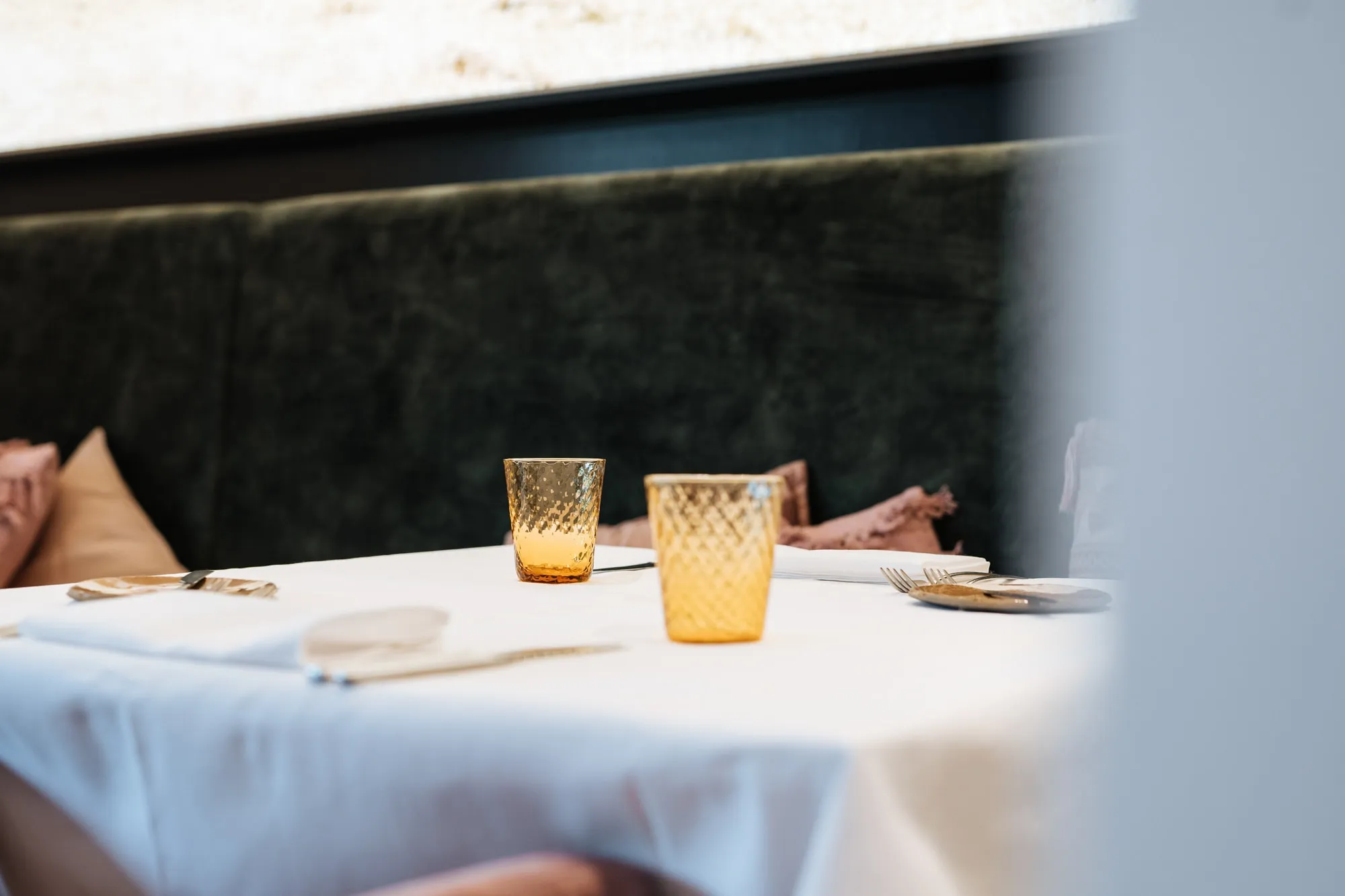 Amberkleurige glazen op een tafel met wit linnen, voor de donkergroene bank