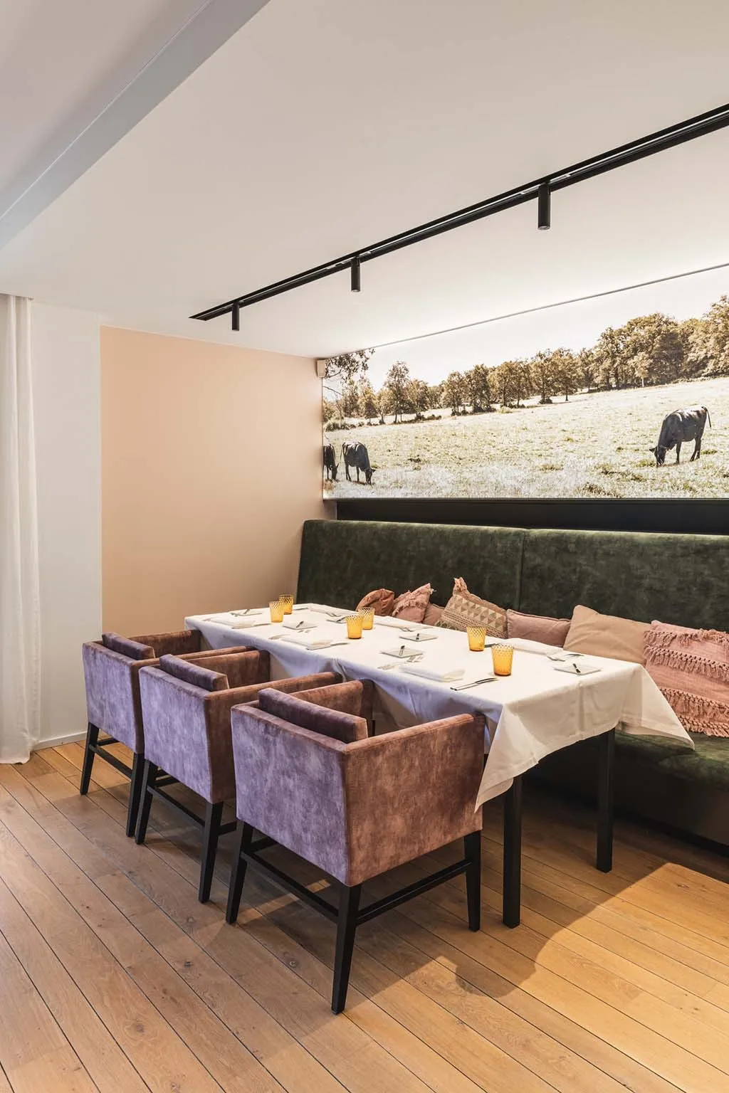 Een hoektafel met mauve fluwelen stoelen aan de groene bank, onder de wandfoto van de runderen