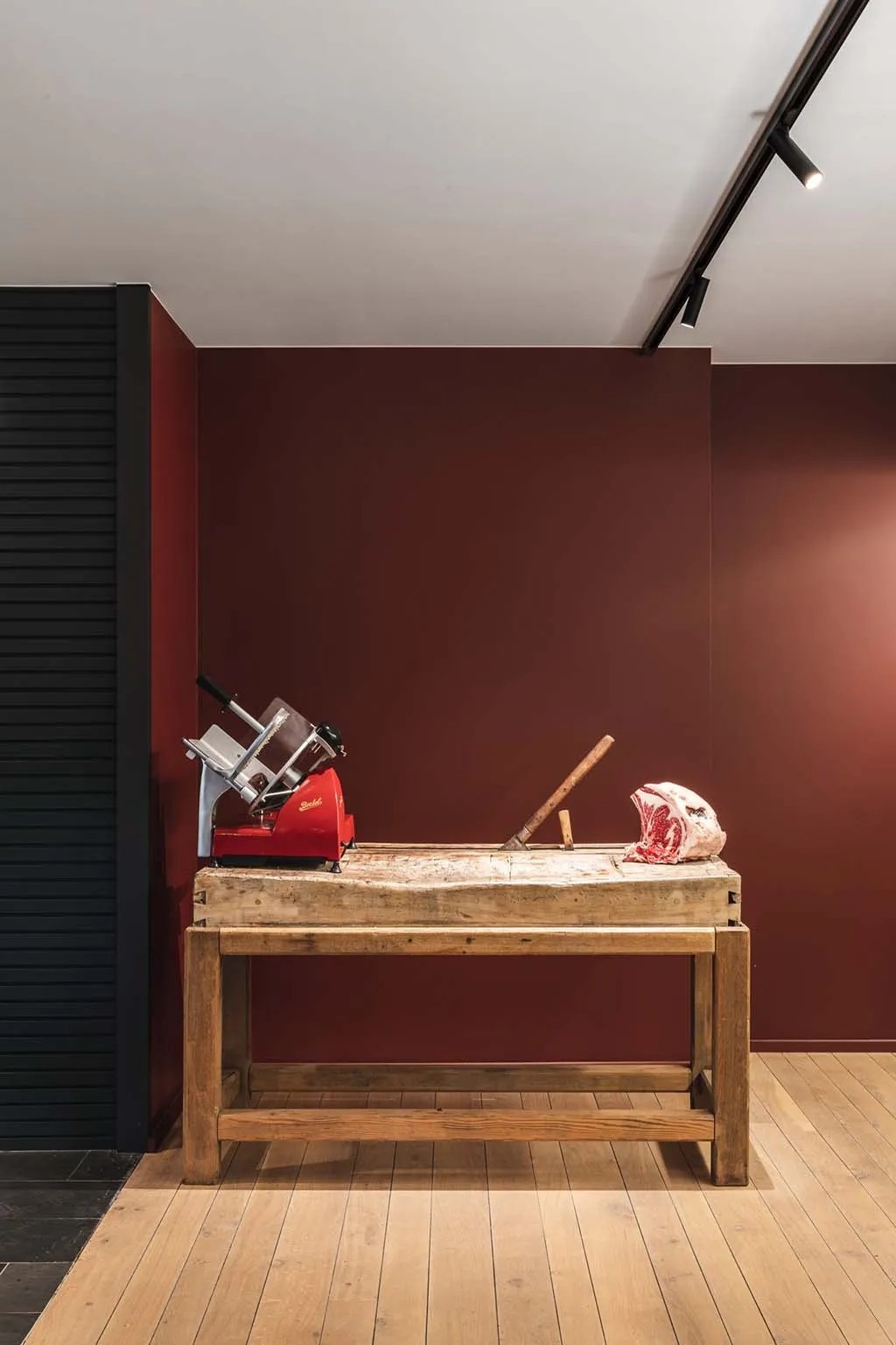 In de winkel: een houten kapblok met een rode snijmachine en een stuk vlees, voor de bordeauxrode muur